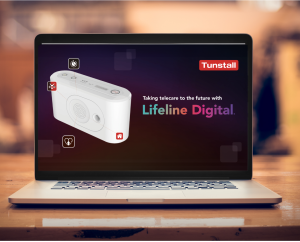 A laptop computer displaying a Tunstall healthcare product on a black background. The text reads 'taking telecare to the future with Lifeline Digital. The laptop is on a wooden desk.