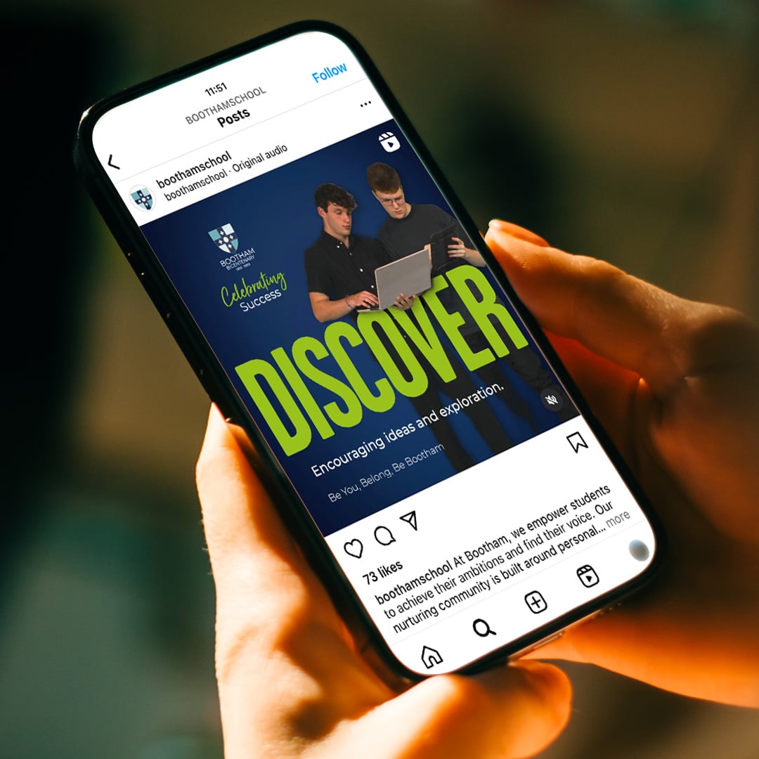 Mobile phone displaying an Instagram post of two teenage school boys stood with a laptop against a dark blue background. The word Discover is in bright green across the front of the image.